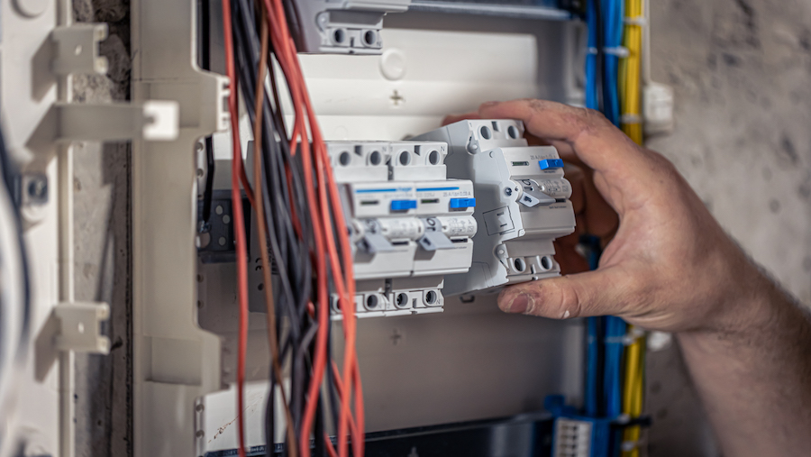 A male electrician works in a switchboard with an electrical connecting cable.