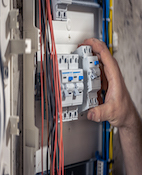 A male electrician works in a switchboard with an electrical connecting cable.